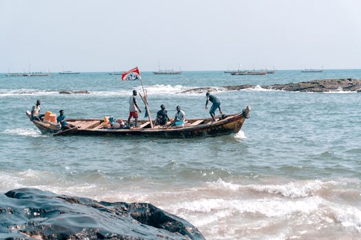 Fishermen navigating a wooden boat on the vibrant Elmina coast, showcasing traditional fishing culture in Ghana.